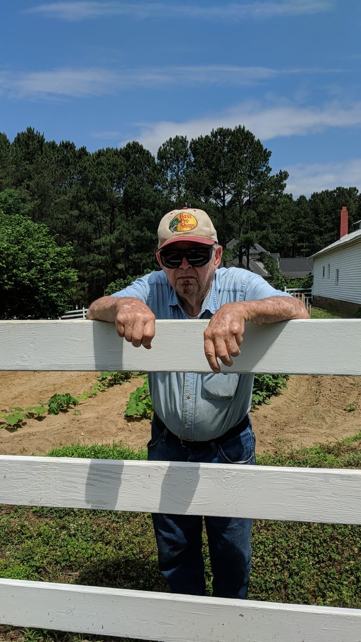 The owners' grandfather leaning on a white three-rail farm fence in Zebulon, NC